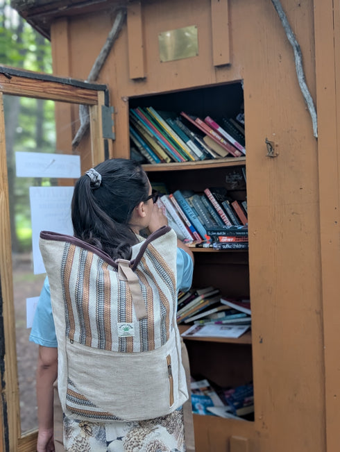 Person with a backpack looking into a wooden bookshelf filled with books outdoors.